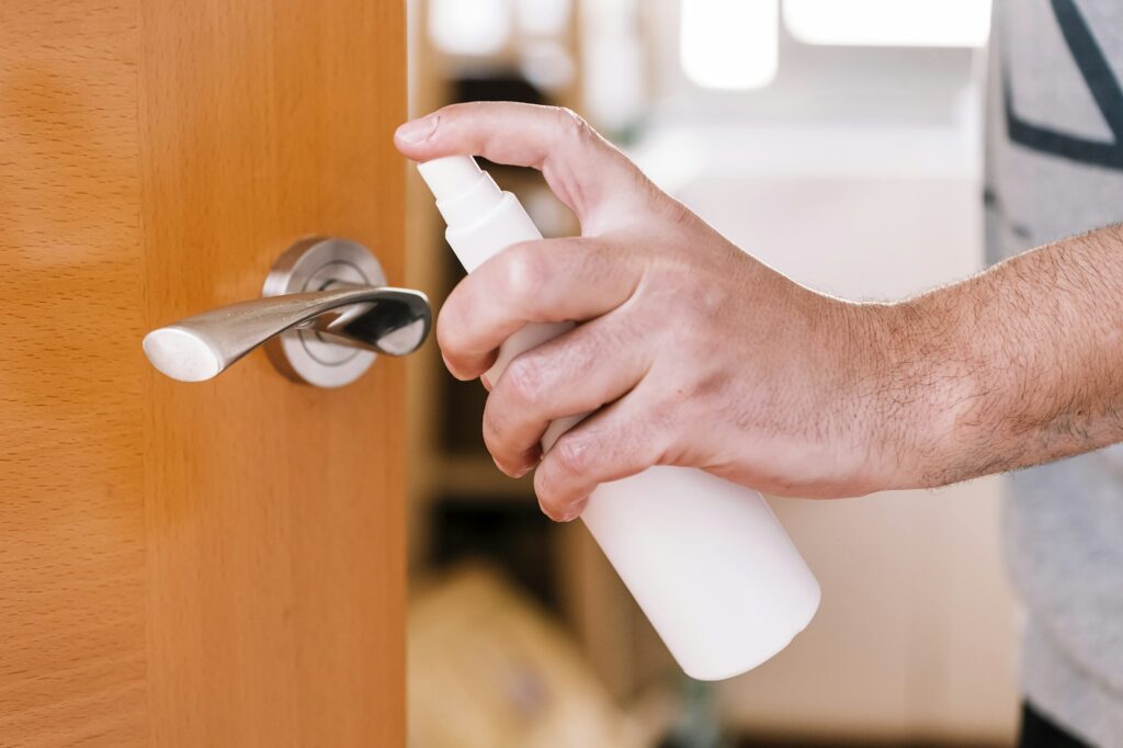 hand sanitizing a doorknob with disinfectant spray